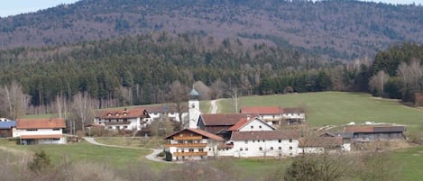 Un pueblo rural con edificios tradicionales, una iglesia y una colina al fondo.