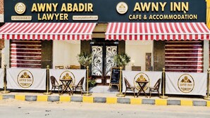 A cafe with a red and white striped awning, outdoor seating with tables and chairs, and a sign indicating it's a lawyer's office. - AWNY INN - Luxury Boutique Apartment & Café⁠ (El Qoseir⁠)