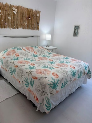 A bed with a floral bedspread, a bedside table with a lamp, and a wall-mounted decorative piece. - Beautiful Vacation Home with Saltwater Pool, Lake View and SW Exposure (Naples)