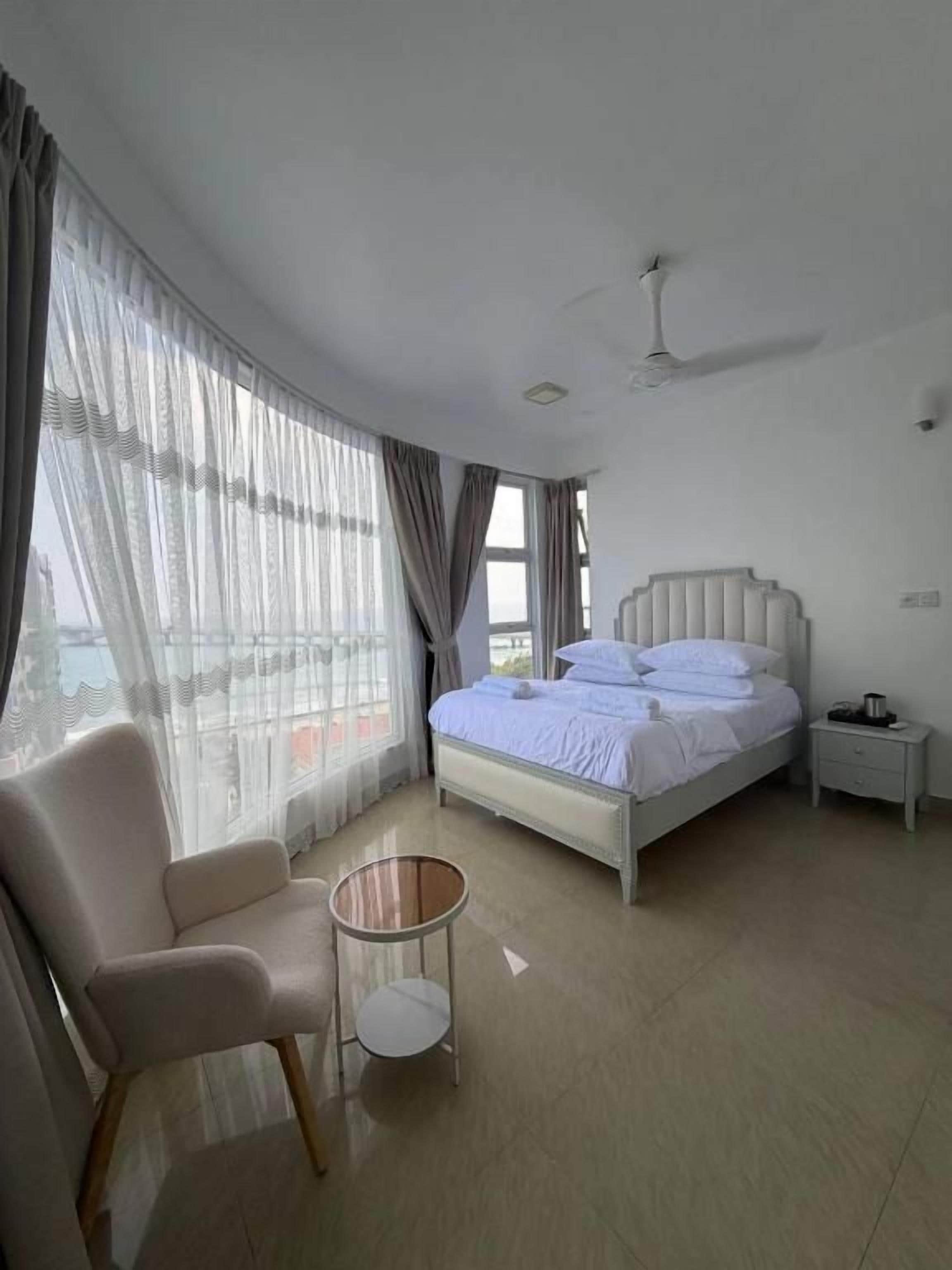 A bedroom with a bed, a chair, a bedside table, and a ceiling fan.