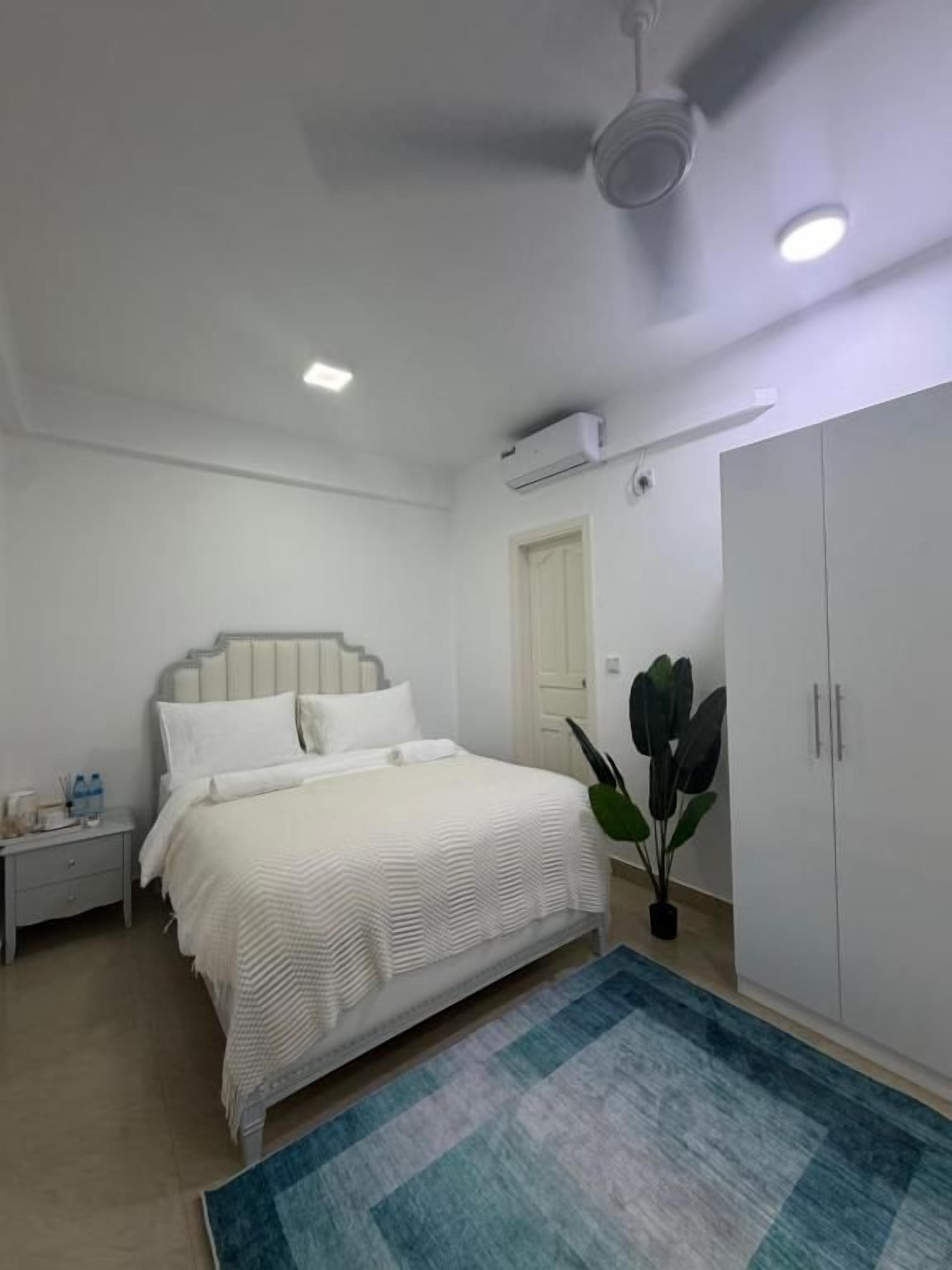 Une chambre à coucher comprenant un lit, une table de chevet, une armoire et un ventilateur de plafond.