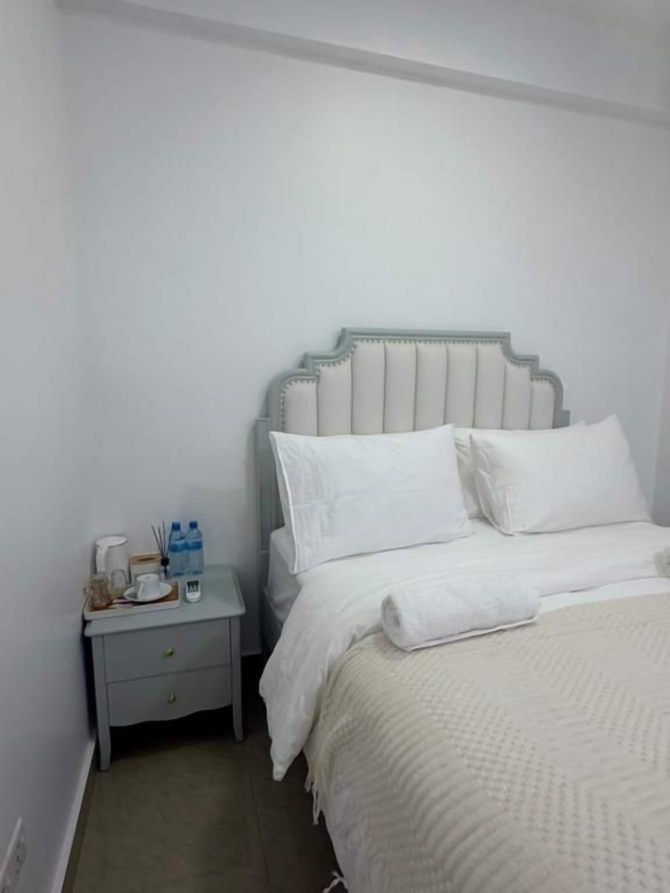 A single bed with a headboard, a bedside table with a lamp, and a nightstand with a bottle and glasses.