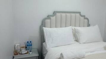 A single bed with a headboard, a bedside table with a lamp, and a nightstand with a bottle and glasses.