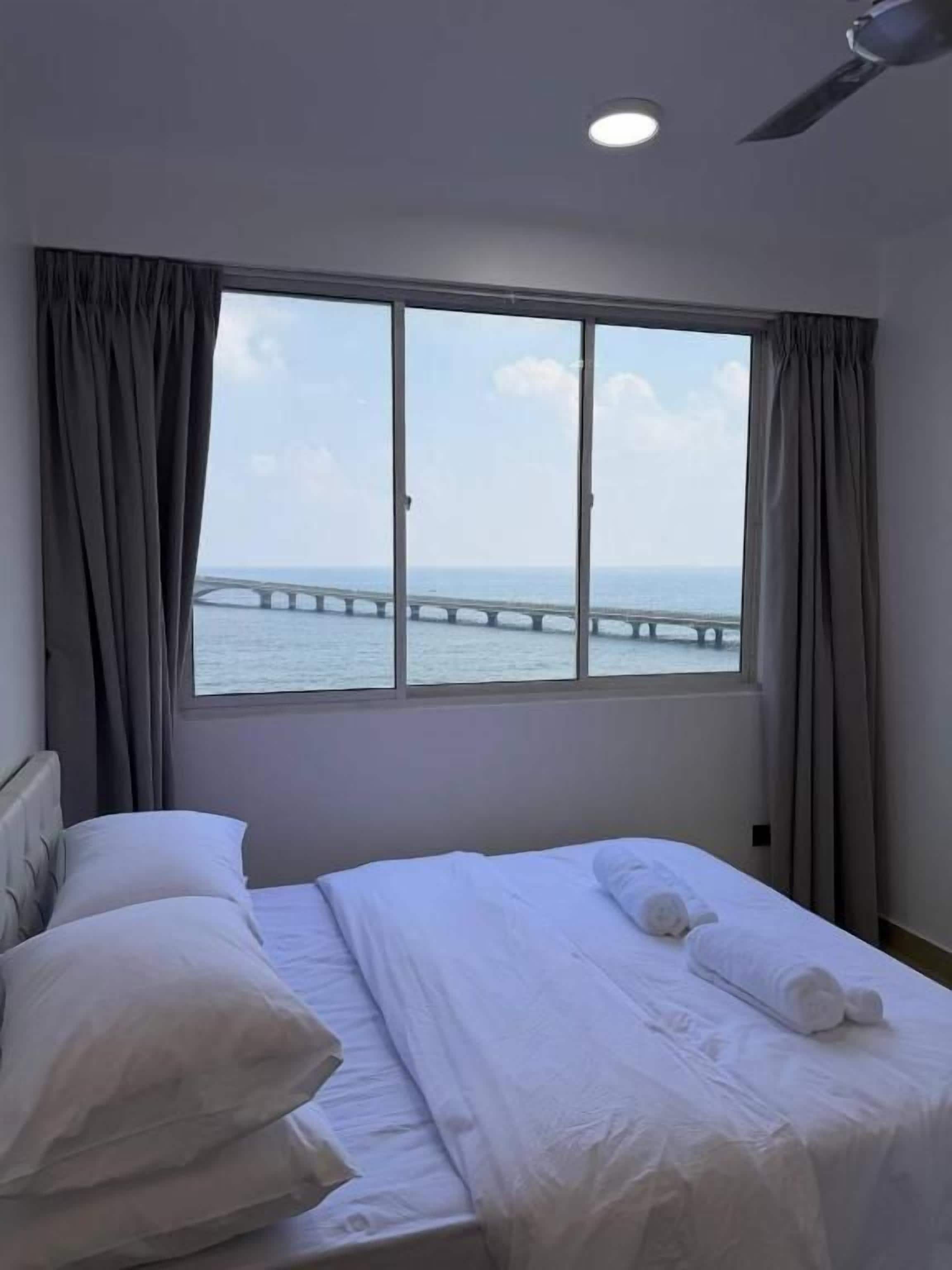 A hotel room with a large window, a bed with white linens, and a view of a bridge over water.