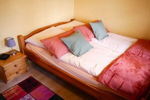 Un lit simple avec un cadre en bois, une table de chevet avec une lampe et un tapis coloré.