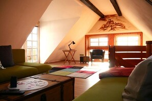 Une pièce mansardée chaleureuse avec un plafond en pente, un canapé vert, une table en bois avec une télécommande et un tapis coloré.