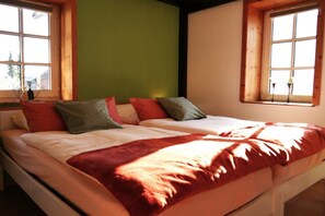 Ein Bett mit vielen Kissen und einer Decke, ein Fenster mit Ausblick und eine grüne Wand.