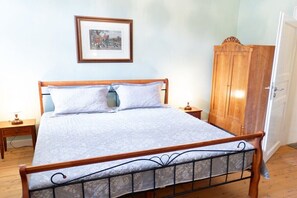 Een slaapkamer met een houten bed, een nachtkastje, een kledingkast en een lijst met een afbeelding aan de muur.