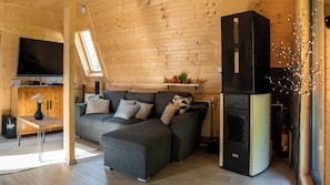 A cozy cabin interior with a sectional sofa, a flat-screen TV, a black refrigerator, and a wooden ceiling.