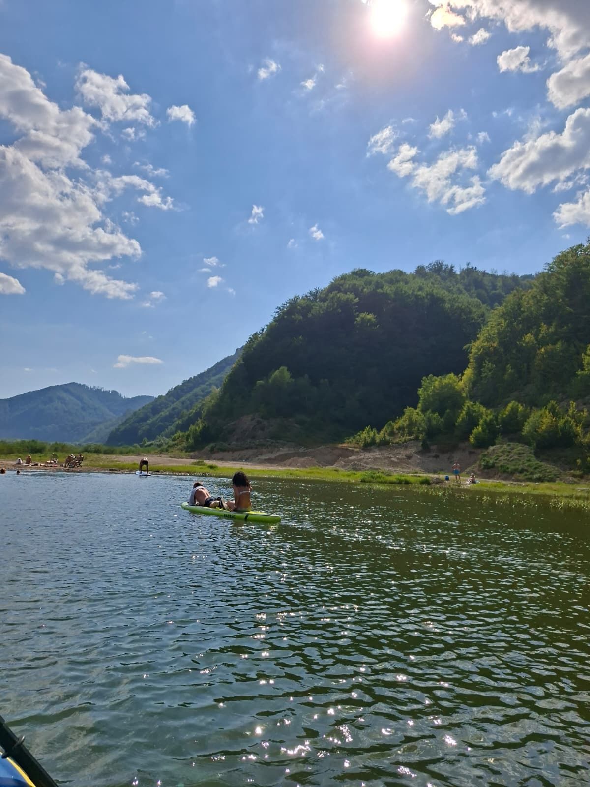 A river with people on a green raft, surrounded by hills and trees.