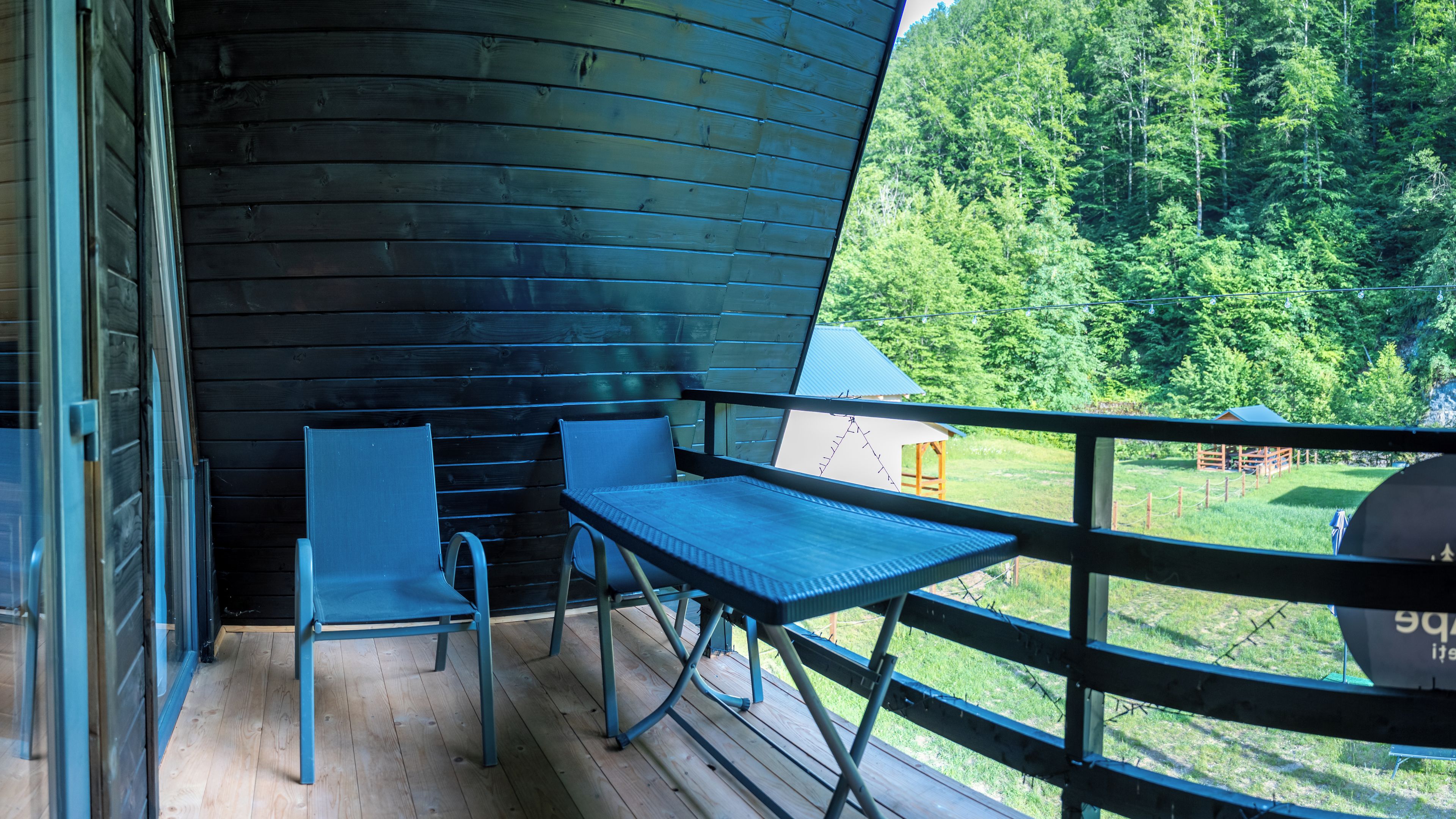 A balcony with a table and chairs, overlooking a forested area.