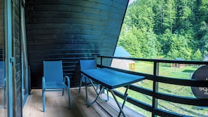 A balcony with a table and chairs, overlooking a forested area.