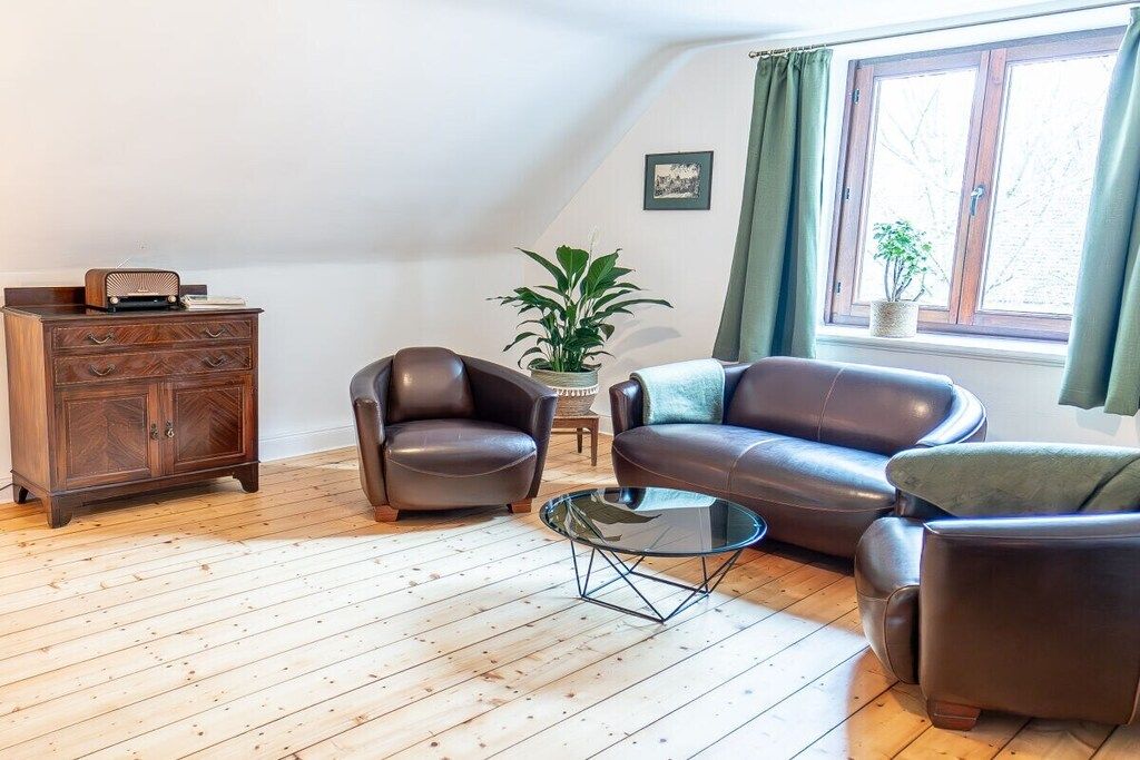 A living room with a brown leather sofa, a brown leather armchair, a glass coffee table, and a wooden cabinet.