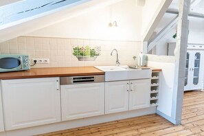 A kitchen with white cabinets, a wooden countertop, a built-in dishwasher, a hanging plant, and a window above the sink. - Vlatten Manor House - Under the Roof (Heimbach)
