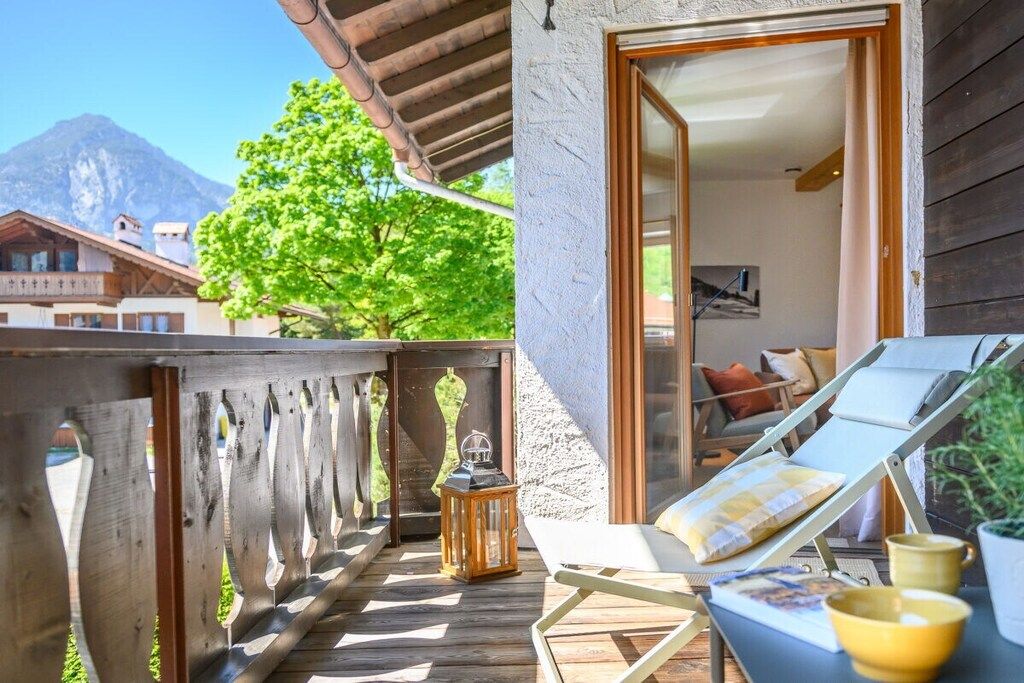 Un balcon en bois offrant une vue sur une montagne, avec une chaise et une table sur laquelle est posée une lanterne.