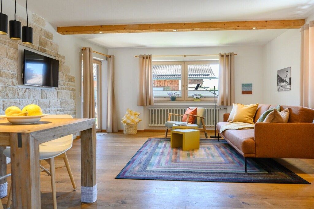 Ein gemütliches Wohnzimmer mit einem Holzesstisch, einer Couch und einem an einer Steinwand befestigten Fernseher.