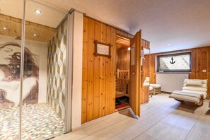 Ein Holzinnenraum mit Sauna, einer Duschkabine aus Glas und einem Fernseher, der ein Ankerbild zeigt.