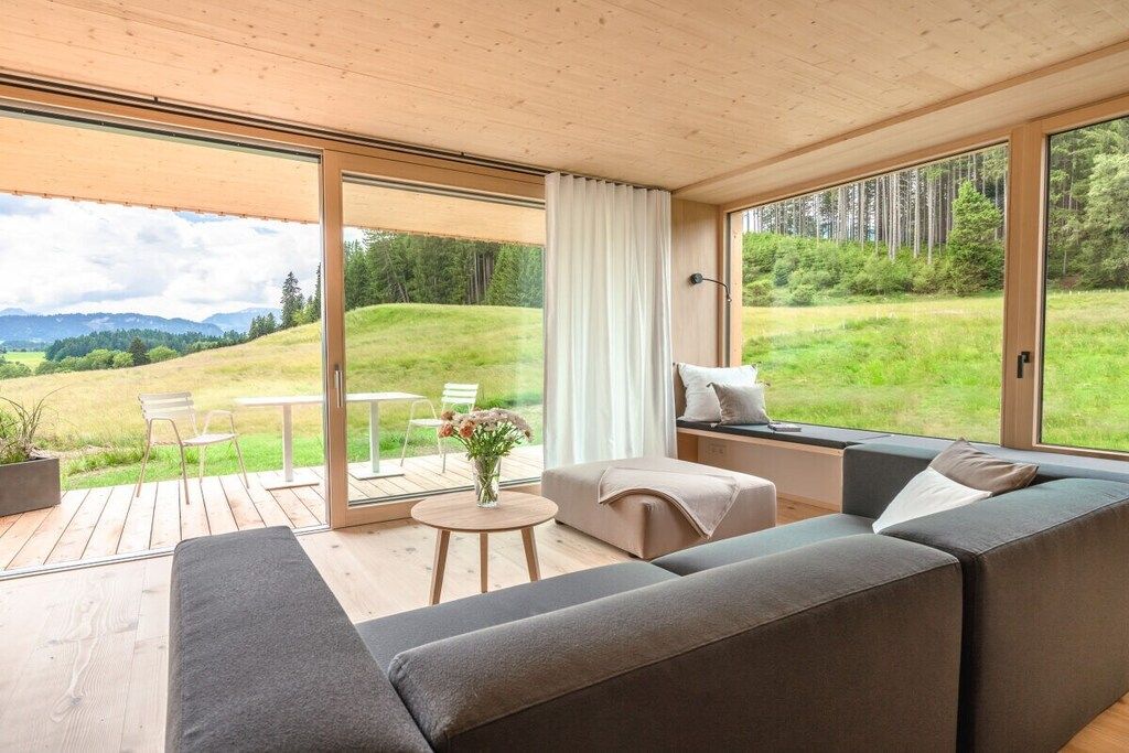 A modern interior with a sofa, a small table, and a window overlooking a grassy landscape.