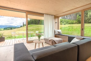 Un intérieur moderne avec un canapé, une petite table et une fenêtre donnant sur un paysage verdoyant.