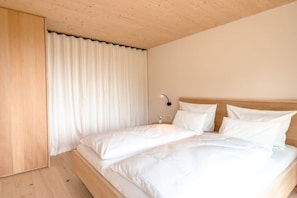 A bedroom with a wooden ceiling, a bed with white bedding, and a nightstand with a lamp. - Holiday apartment Wald (Bolsterlang)