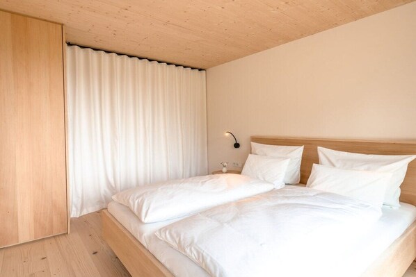 Une chambre avec un plafond en bois, un lit avec une literie blanche et une table de chevet avec une lampe.