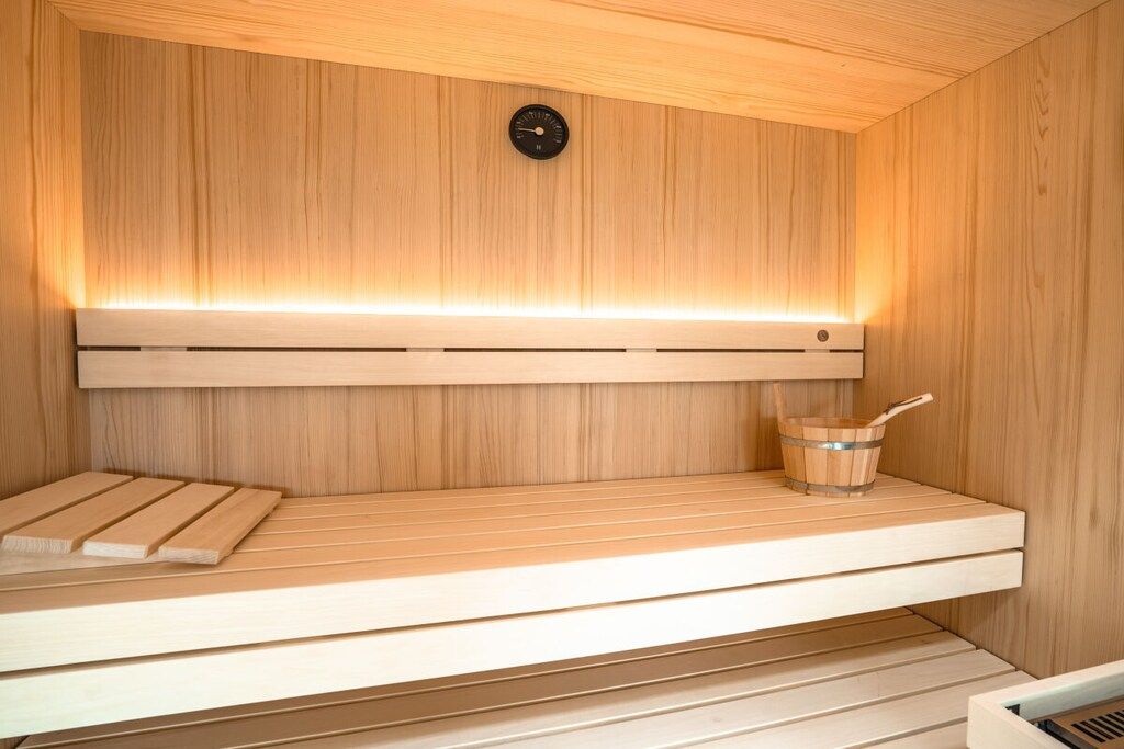 A wooden sauna with a bench, a bucket, and a control panel.