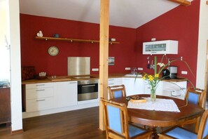 A compact kitchen with white cabinets, a wooden dining table with blue chairs, and a vase with yellow flowers. - Holiday apartment with 1 bedroom (Ratzeburg)