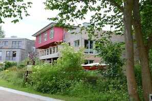 A residential building with a red facade, a balcony, and a boat in the background. - Holiday apartment with 1 bedroom (Ratzeburg)