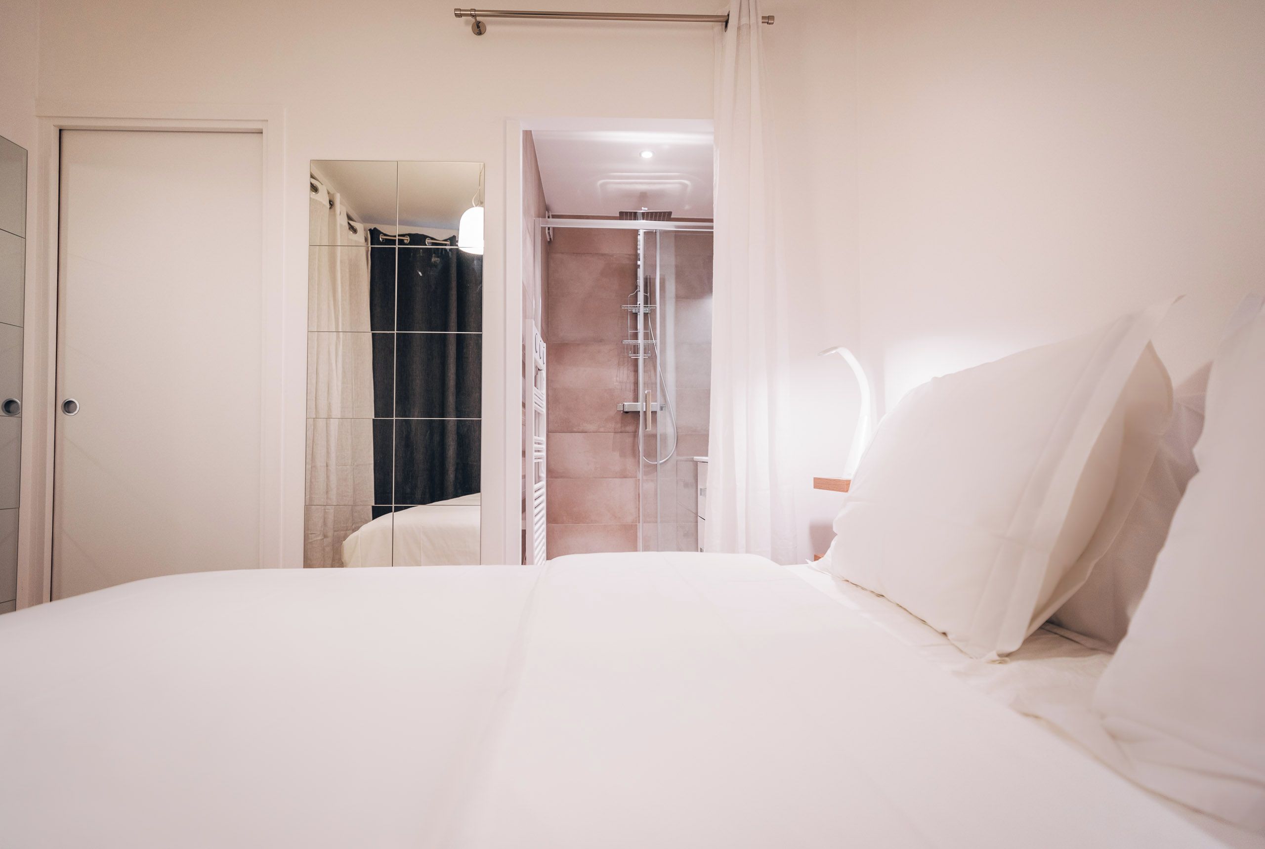 Een hotelkamer met een bed, een douche en een deur naar een andere kamer.