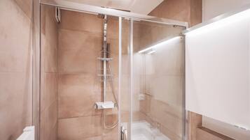 A modern shower enclosure with a glass door, a handheld showerhead, and a wall-mounted faucet.