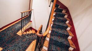 Uma escada de madeira com corrimão, degraus carpetados e uma parede vermelha.