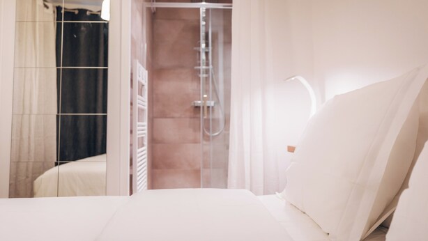 Casa de banho moderna com chuveiro, espelho e cama com roupa de cama branca.