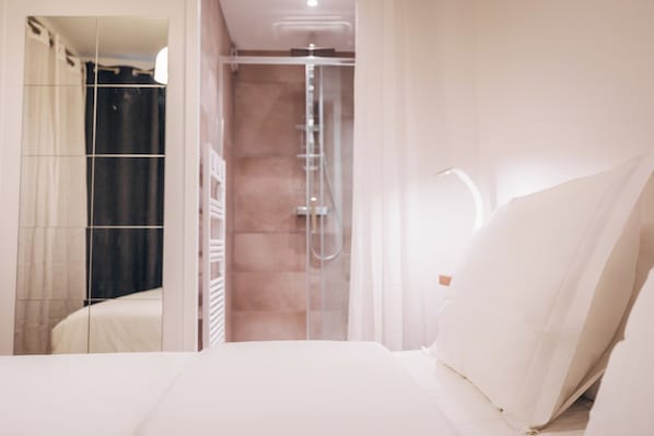 Een moderne badkamer met een douche, een spiegel en een bed met wit beddengoed.