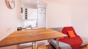 Um espaço de estar compacto com uma mesa de jantar de madeira, cozinha compacta, guarda-roupa embutido e sofá com manta vermelha.