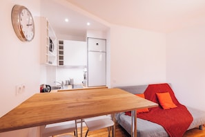 Een compacte leefruimte met een houten eettafel, een kitchenette, een inbouwkast en een bank met een rode plaid.
