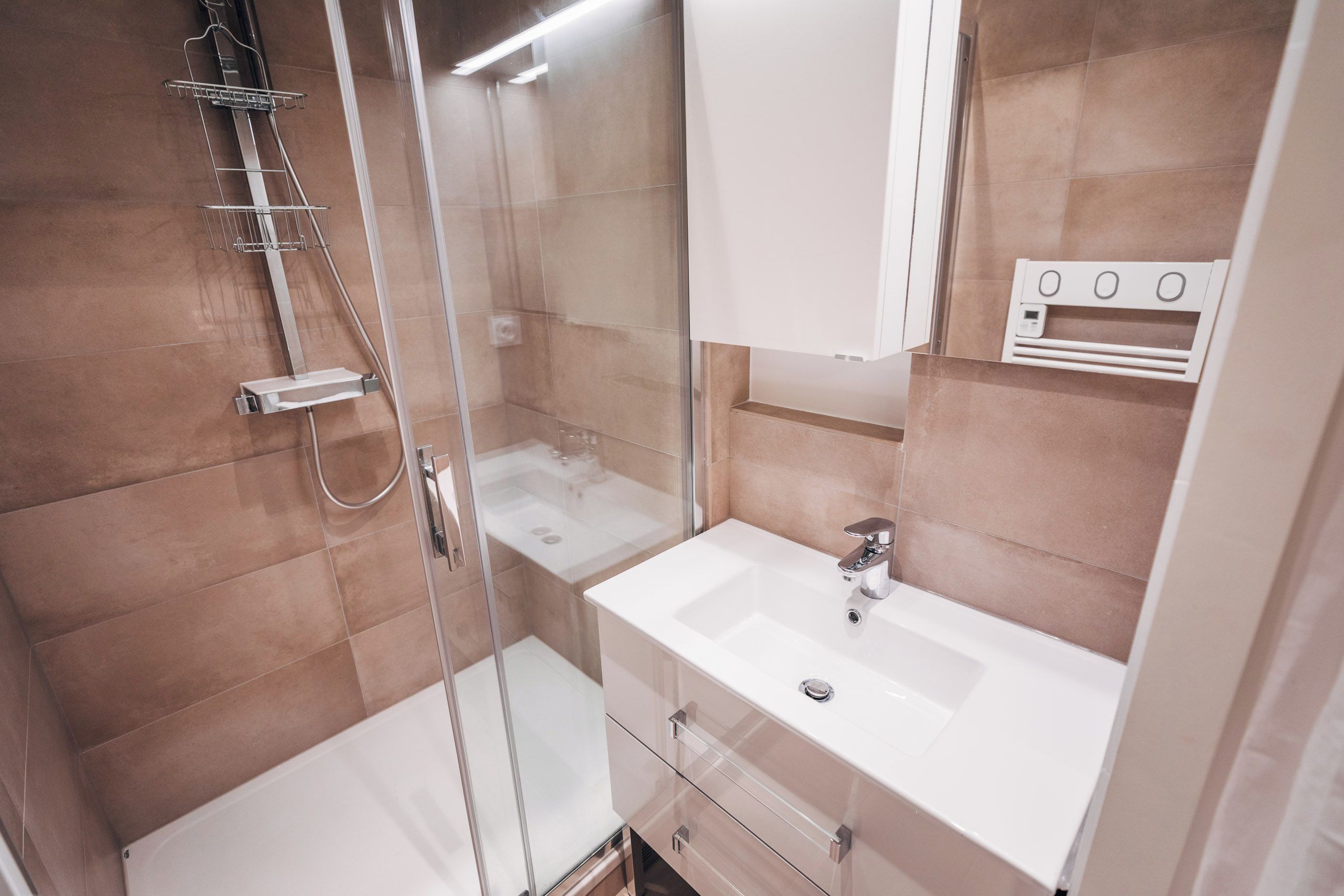 Een moderne badkamer met een douchecabine van glas, een witte wastafel en een spiegel erboven.