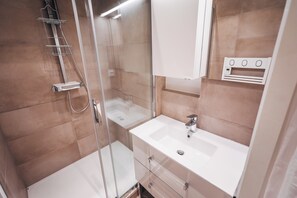 A modern bathroom with a glass shower enclosure, a white sink, and a mirror above it.