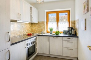 Une cuisine avec des meubles blancs, un plan de travail noir, une fenêtre avec des rideaux et une cuisinière.