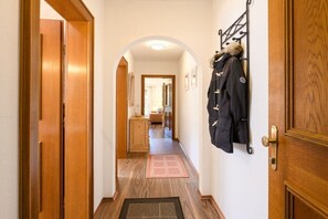 Ein Flur mit Holzboden, einem Kleiderständer mit Jacken und einer Tür rechts.