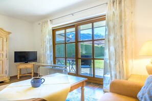 Ein Zimmer mit Fernseher auf einer Holzkommode, einem Tisch mit einer Tasse und einem großen Fenster mit Blick auf Grünflächen und Berge.