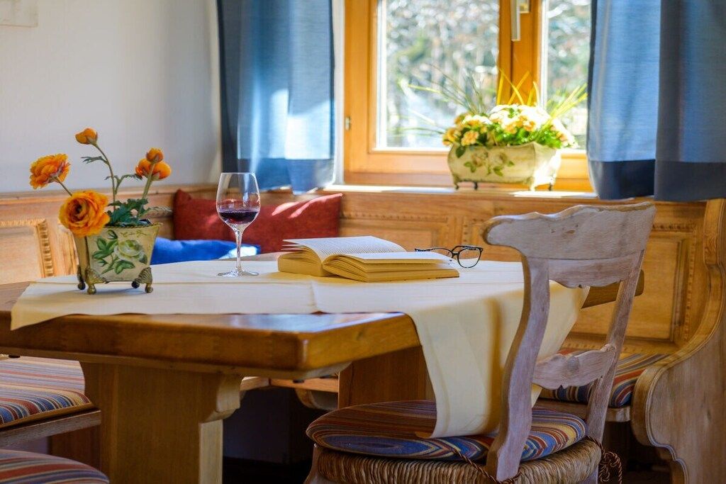 A wooden table with a book, a glass of red wine, and a vase with flowers.