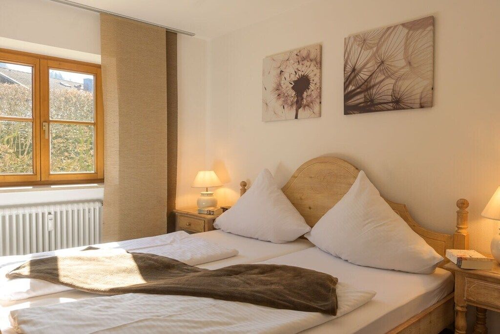 Une chambre d’hôtel comprenant un lit, deux lampes de chevet, une fenêtre avec des rideaux et deux œuvres d’art murales.