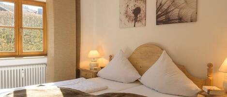 A hotel room with a bed, two bedside lamps, a window with curtains, and two wall art pieces.