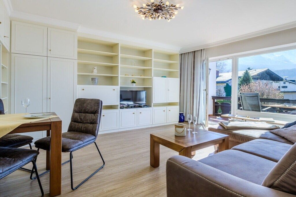 A modern living room with a sofa, a dining table, and a kitchen area with cabinets and a refrigerator.