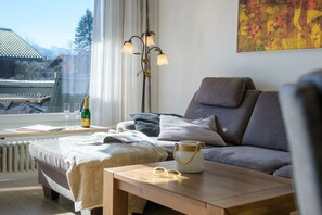 Ein modernes Wohnzimmer mit einer Couch, einem Tisch mit Gläsern und einer Flasche, einem Heizkörper und einem Fenster mit Vorhängen.