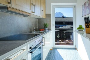 A modern kitchen with a built-in oven, a sink, and a view of a traditional building through an open door. - Holiday apartment with 1 bedroom (Garmisch-Partenkirchen)