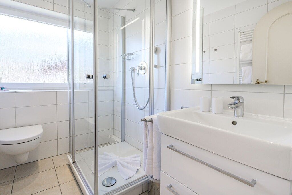 A modern bathroom with a glass-enclosed shower, a white sink, and a mirror above the sink.