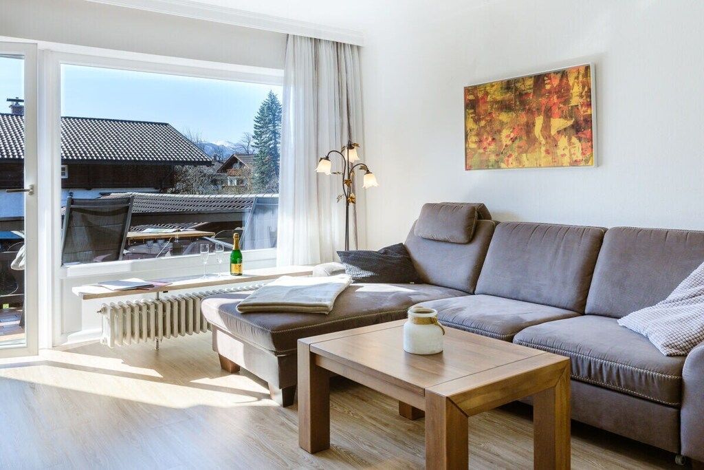 Uma sala de estar moderna com um sofá, uma mesa de centro e um radiador. Há uma janela com vista para casas e árvores.