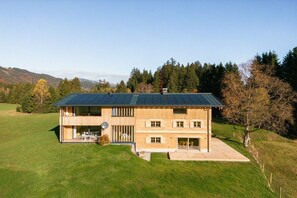 A two-story house with a flat roof and a balcony, surrounded by a grassy field and trees. - Holiday apartment Himmel (Bolsterlang)