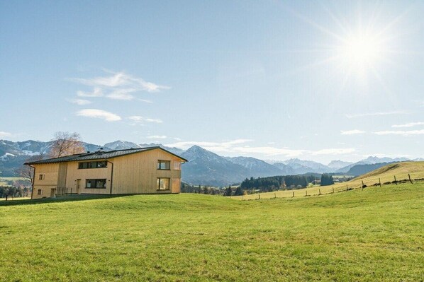 Una casa de fusta de dos pisos amb un gran jardí davant i muntanyes al fons.